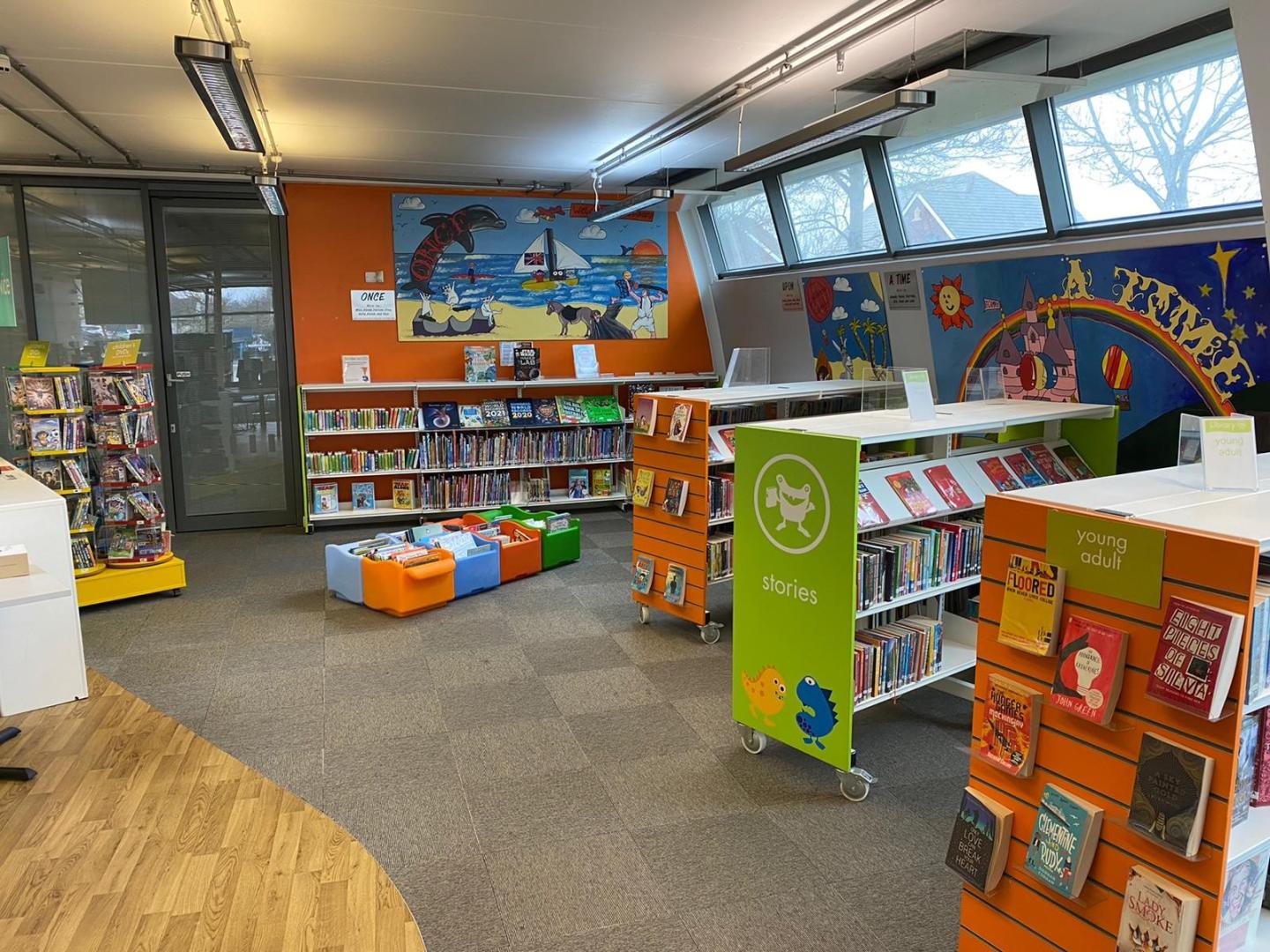 An interior of a children's area at a library, with colourful paintings on the walls and books on the shelves